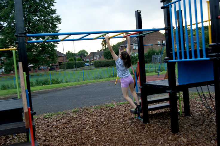 A girl swinging on monkey bars in a play area.